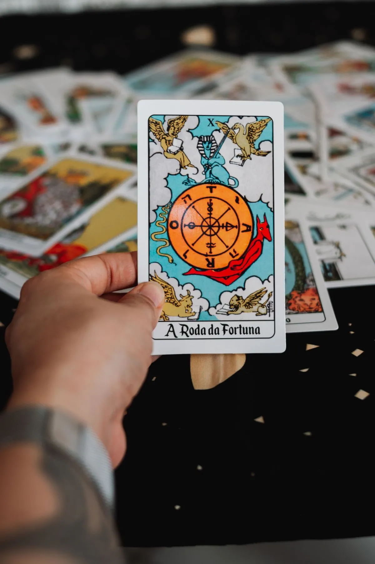 A hand holding a single tarot card above a scattered deck