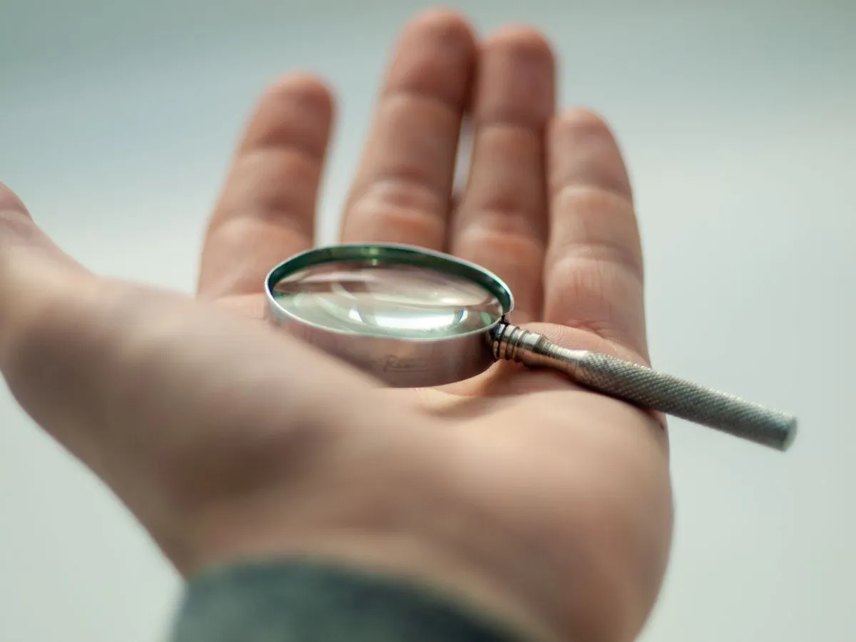 A hand holding a magnifying glass in close, focused examination